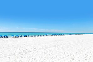 A wide sandy beach with blue umbrellas and lounge chairs.