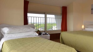 Ett hotellrum med två sängar, ett fönster med utsikt över grönområden och ett nattduksbord med en lampa.