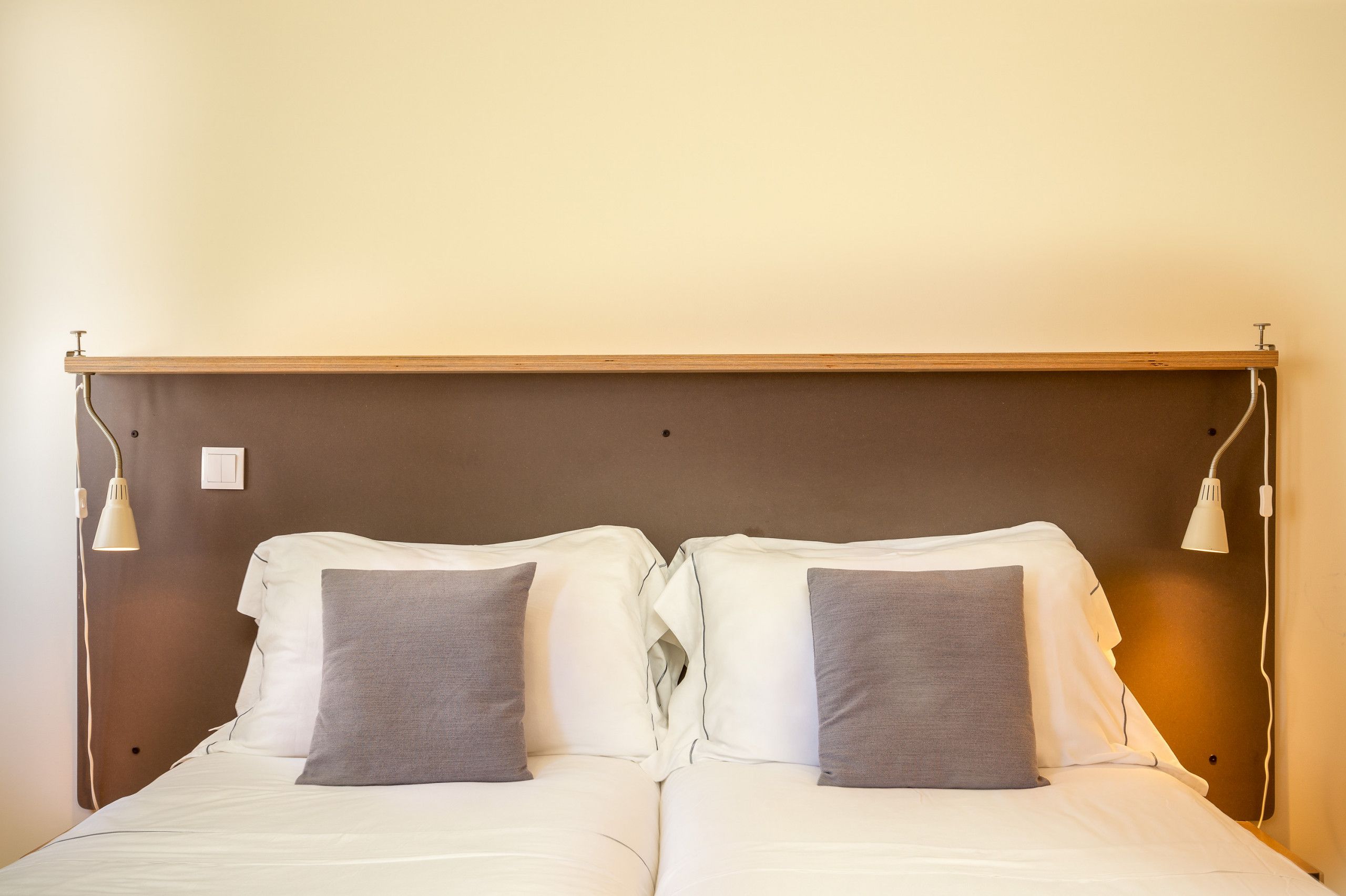 A double bed with white linens and two gray pillows, a wooden headboard, and two bedside lamps.