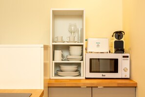 Una cocina con microondas y una alacena con cuencos, tazas y un vaso.