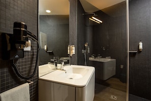 Une salle de bain moderne dotée d’un grand lavabo, d’un miroir, d’un sèche-cheveux et d’un espace douche.