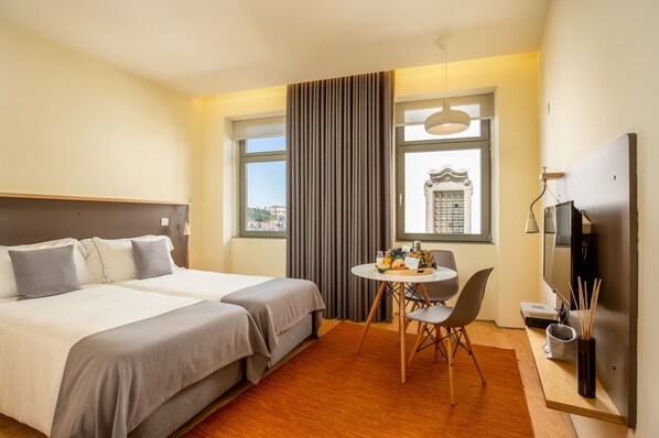 A hotel room with two beds, a dining table, chairs, a TV, and a window with curtains.