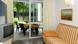 A living room with a sofa, a television, and a sliding glass door leading to an outdoor dining area.