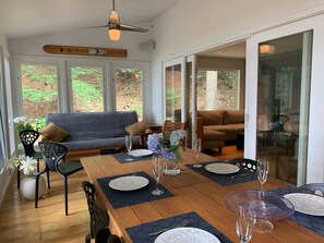 A dining area with a wooden table set for four, surrounded by a gray sofa and a brown couch. - Modern Lake House on Secluded Cove with Private Peninsula  (Enfield)