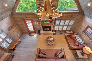 L’intérieur chaleureux d’un chalet en bois comprend une cheminée, un canapé en cuir et un grand lustre fait de bois de cerf.