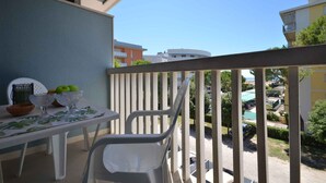 Un balcone con un tavolo apparecchiato per due persone, sedie e una ciotola di frutta.