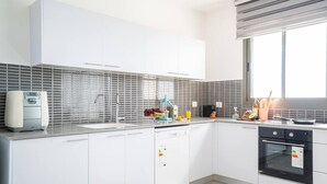 A modern kitchen with white cabinets, a dishwasher, an oven, and a window providing natural light. - Panoramic Sea Views Coastal Escape by Sea N' Rent (Nahariya)
