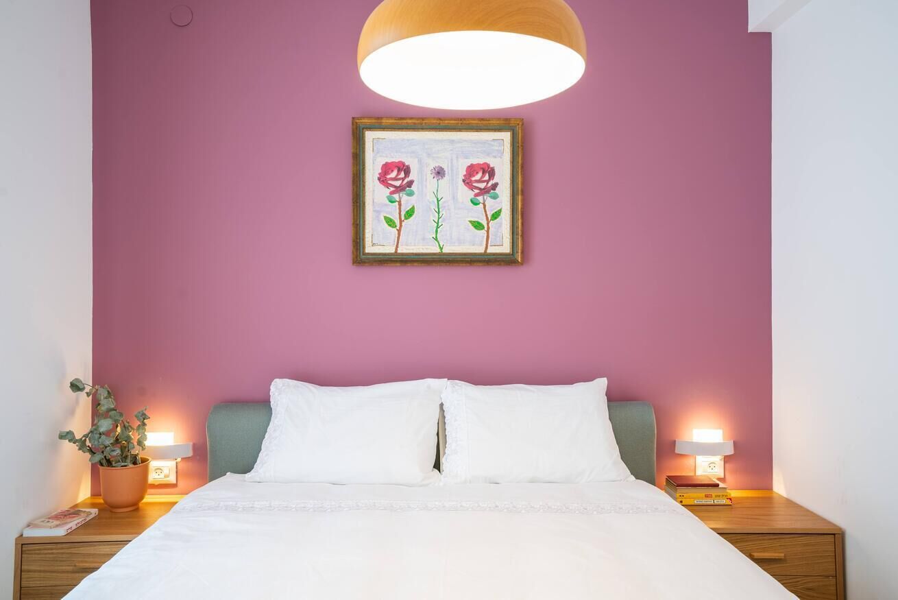 A bedroom with a bed, two bedside tables, a nightstand, a potted plant, and a wall-mounted painting.