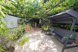 A covered patio area with a swing chair, potted plants, and a cushioned seating area.