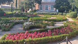 A garden with a variety of flower beds and a building with arched windows in the background.