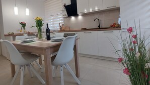 A modern kitchen with white cabinets, a wooden dining table, and pendant lights.