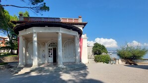 A white pavilion with columns and a tiled roof, located near a body of water.