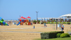 Un parque infantil junto a la playa con toboganes y estructuras de juego, un área de descanso cubierta y cielo despejado.