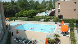 Una piscina en la azotea con dos áreas separadas, rodeada de sillones y sombrillas.