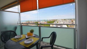Un balcon avec une table dressée pour deux personnes, une plante en pot et une vue sur la ville.