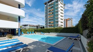 Un hôtel moderne doté d’une piscine sur le toit, de chaises longues bleues et d’un grand immeuble en arrière-plan.