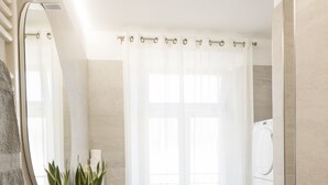 Un bagno moderno con un lavandino ovale, uno specchio, una pianta in vaso, una tenda da doccia e una lavatrice.