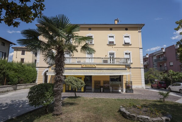 Un edificio de dos pisos con fachada amarilla, un balcón con barandillas blancas y un letrero que dice 'Talmudoteca Firenze'.
