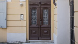 Una porta doppia in legno con un pannello decorativo in vetro, incassata in una porta ad arco, affiancata da un muro semplice e un arco bianco.
