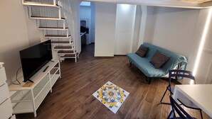 Ett modernt vardagsrum med tv, soffa och en trappa som leder upp till köket.