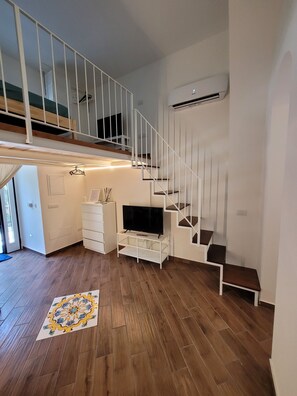 A modern apartment with a wooden floor, a white staircase, a flat-screen TV on a white stand, and a small white dresser. - L&F Apartment - Leonardo Room (Minori)