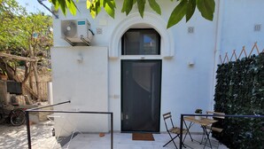 En vit byggnad med en svart dörr, ett litet utomhusområde med sittplatser, stolar och ett bord, samt en Hisense-luftkonditioneringsenhet som är monterad på väggen.