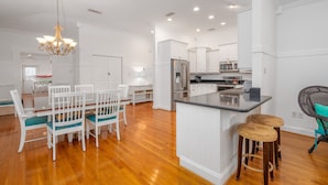 A modern kitchen with white cabinetry, stainless steel appliances, and a central island with bar stools. - Contemporary Beach Home Near Back River for the Whole Crew by Tybee Cottages (Tybee Island)