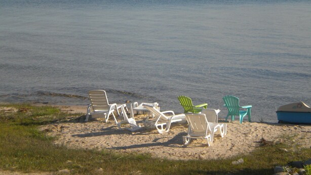 A beach with several white and green lounge chairs and a blue boat on the sand. - Charming cottage with shared beachfront on Grand Traverse Bay near Northport. (Northport)