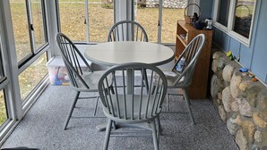 A covered patio with a round table and four chairs, a stone wall, and a view of a residential area. - Charming cottage with shared beachfront on Grand Traverse Bay near Northport. (Northport)