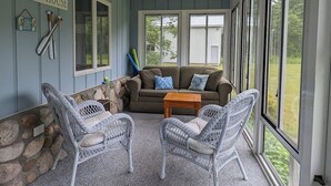 A covered porch with wicker furniture, a couch, and a stone wall. - Charming cottage with shared beachfront on Grand Traverse Bay near Northport. (Northport)