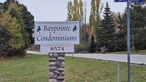 A sign for Bay Pointe Condominiums with a stone pillar base and a street sign in the background. - Charming cottage with shared beachfront on Grand Traverse Bay near Northport. (Northport)