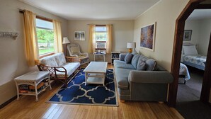 Un salón amplio con un tapete azul estampado, dos sofás, un sillón de mimbre y una mesita.