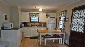 Una cocina compacta con armarios blancos, una mesa de comedor de madera y un refrigerador.