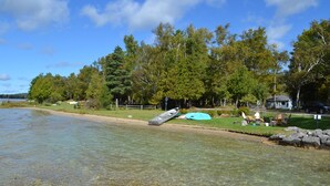 A lakeside property with clear water, a sandy beach, and a row of trees.