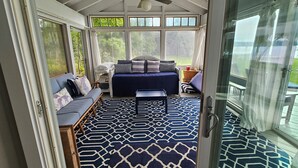 A cozy room with a bed, a sofa, and a dining table, featuring large windows and a patterned rug.