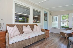 Una habitación acogedora con un sofá de mimbre, una mesa de madera y ventanas amplias que ofrecen vistas al exterior.