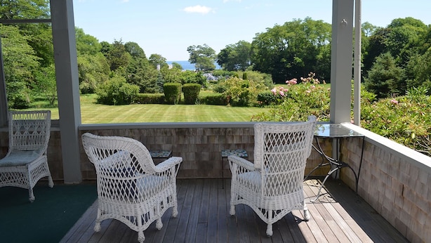 Eine überdachte Terrasse mit Korbstühlen und einem Tisch, mit Blick auf einen gepflegten Rasen und Garten.