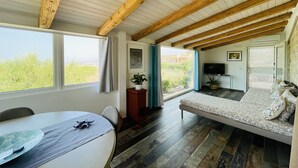 Habitación con techo de madera, cama con ropa de cama estampada, televisor y vista a zonas verdes.