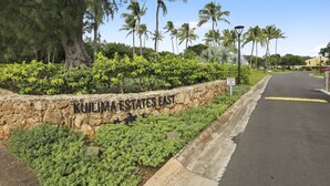 A stone wall with "KULIMA ESTATES EAST" written on it, surrounded by lush greenery and palm trees. - Turtle Bay Heliconia. (Kahuku)