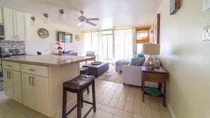 A modern kitchen with a central island, a dining area with a sofa, and a living room with a TV. - Turtle Bay Heliconia. (Kahuku)