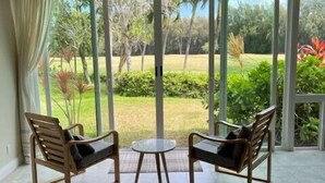 A room with two wooden chairs and a small table, large glass doors leading to a garden. - Turtle Bay Heliconia. (Kahuku)