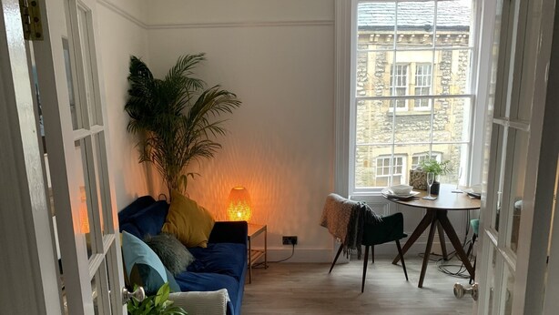 A cozy living room with a blue sofa, a large potted plant, and a table with chairs. - Beautiful 1-bed Apartment in Kirkby Lonsdale (Carnforth)