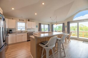 A spacious kitchen with a central island, wooden bar stools, and large windows offering a view of the outdoors. - Time to Chill - Corolla, Whalehead, Ocean View, 480 Yds to Beach, Pool, Flex Stays (Corolla)