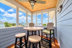 A covered patio with a table and chairs, large windows, and a ceiling fan. - Time to Chill - Corolla, Whalehead, Ocean View, 480 Yds to Beach, Pool, Flex Stays (Corolla)