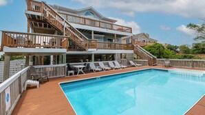 Ein zweistöckiges Haus mit einer Holzdachterrasse, einem Schwimmbecken und Sitzgelegenheiten im Freien.