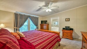 Een slaapkamer met een bed, een plafondventilator, een dressoir, een spiegel en een raam met gordijnen.