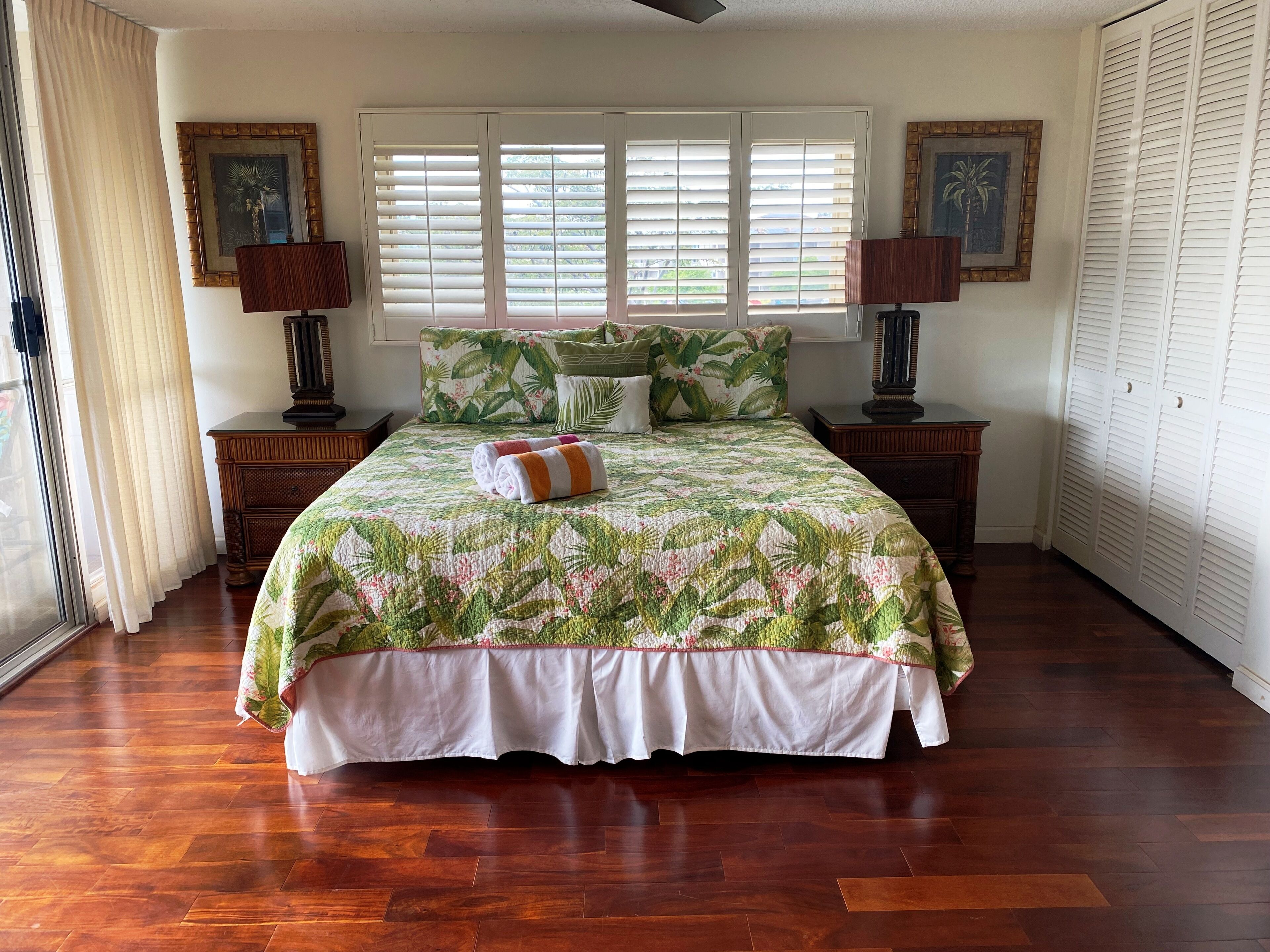 A bedroom with a large bed, a window with blinds, wooden nightstands, and two wall-mounted lamps.