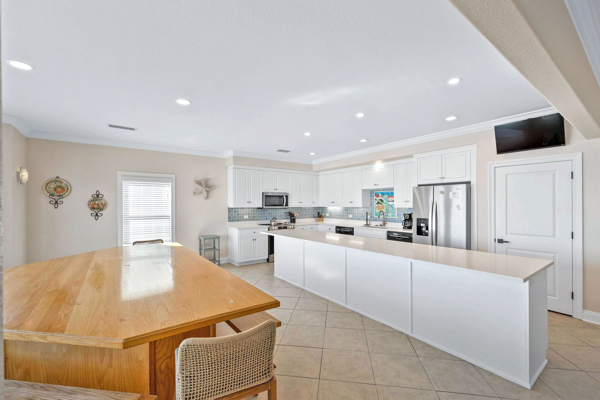 A modern kitchen with white cabinetry, a central island, stainless steel appliances, and recessed ceiling lights.