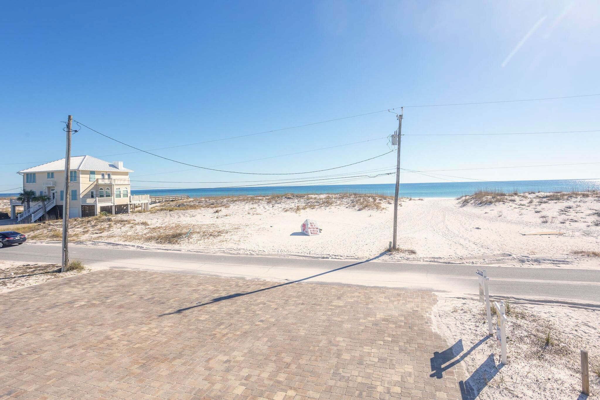 A beachside property with a paved walkway, a building with a white facade, and a clear view of the ocean.