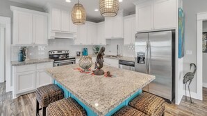 Una cucina moderna con mobili bianchi, una grande isola con posti a sedere, un frigorifero in acciaio inossidabile e oggetti decorativi.
